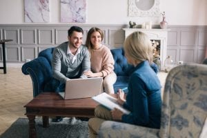 A smiling young couple sitting in their living room with a woman with a Behaviour Therapist having a parent/caregiver coaching session by Side by Side Therapy.